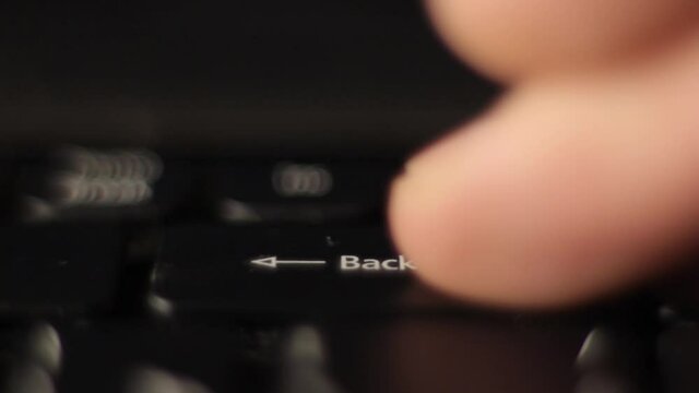The finger presses the backspace button on the keyboard. Close-up.
