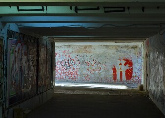 Pedestrian underpass covered with old graffiti. Dirt. Sunlight. Blue light. Inscriptions.