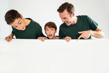 Dad and his two sons pointing on an empty white board, smiling. Studio shot. Real people emotions.