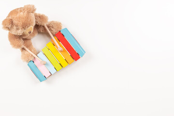 Toy teddy bear playing on colorful xylophone. Kid toys on white background. Early childhood music education. Top view, copy space