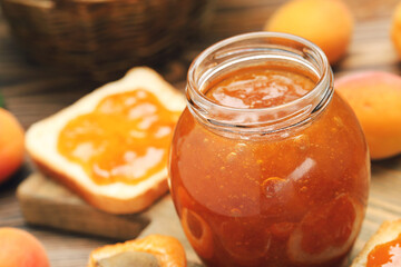 Apricot jam in jar and toast on wooden background