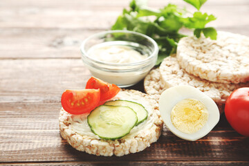 Crispbread with cream cheese, eggs and vegetables on brown wooden table