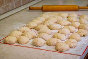 Balls of dough for homemade pies are prepared for rolling out on the table. A wooden rolling pin at the background.