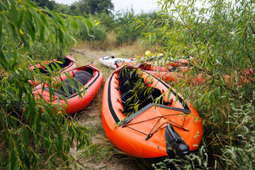 Inflatable red kayak. Active rest, sport, kayak. Boat for rafting on water. There are several kayaks on the shore.