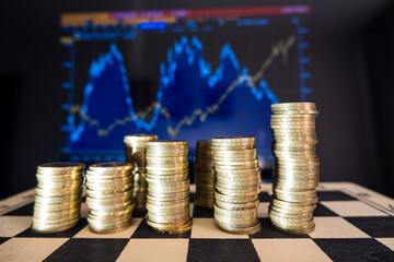 There are columns of coins on the chessboard. On the edge written Belarus. Coins with a face value of 2 rubles. In the background is a blurry stock chart.