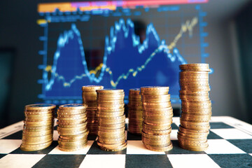 There are columns of coins on the chessboard. On the edge written Belarus. Coins with a face value of 2 rubles. In the background is a blurry stock chart.