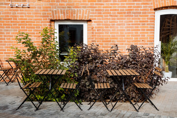 Fototapeta na wymiar Street terrace of the coffee shop. Wooden tables for two next to the coffee shop behind green bushes. Coffee shop in the city center.