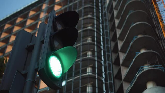 The traffic light is working at the intersection in close-up. Yellow works and switches to green. A skyscraper under construction in the background