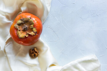 Flat lay style persimmon and walnut in high key on a light painted background with silk cloth 