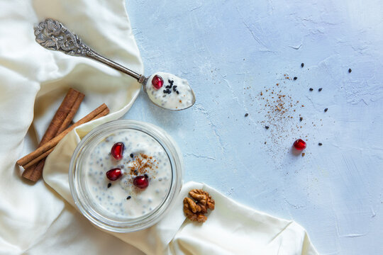Flat lay style high key composition of diary free vegan soy yogurt with chia seeds, cinnamon and pomegranate seeds with silk cloth and silver spoon on a light painted background