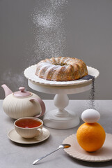 Fresh bundt cake or muffin cake decorated icing sugar with teapot and cup of tea on the table. Sieving powdered sugar on a Christmas cake. Selective focus
