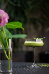 Glass with green matcha sour cocktail decorated with green leaf on background with pink flovers
