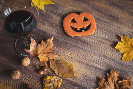 Halloween still life. Glass of red wine, autumn leaves and pumpkin figure with nuts. Halloween decoration on wooden table. Creepy decoration. October still life. The fall season concept.