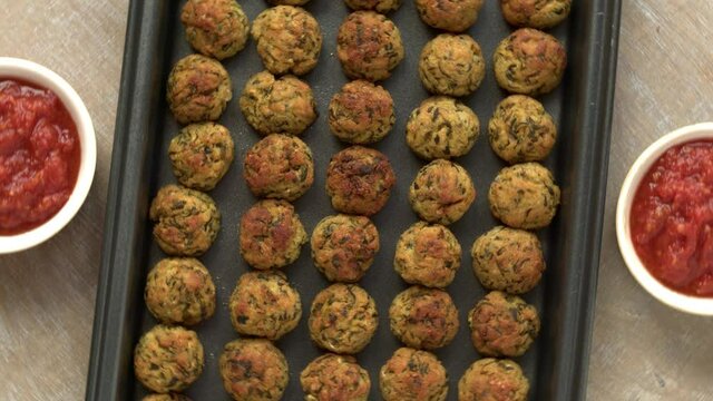Courgette kofta balls on baking tray. Vegan zucchini baked food with tomato sauce. Indian cuisine.