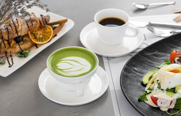 Cup of matcha latte and coffee. High quality photo. Matcha, green tea latte in a cup and croissant. Gray background. Close up. Top view.