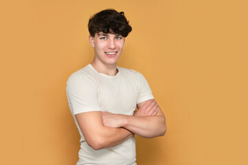 Handsome teenage boy in white t-shirt smiling happily on yellow background. The guy has healthy white teeth, the concept of beauty and health in adolescence