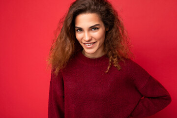 Young beautiful curly brunette woman with sincere emotions poising isolated on background wall with copy space wearing casual dark red sweater. Fun and joy concept