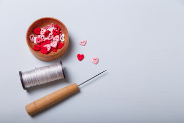 Wooden bowl of heart shaped red and pink buttons with spool of threads and awl for sewing and embroidery on white background. Set of materials for handcraft, making of bijouterie and accessories.