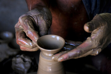 A potter prepares clay Pots or diya on potter's wheel in his residence ahead of Diwali festival. Wet and muddy hands of a craftsman shaping a clay vase on a pottery wheel.