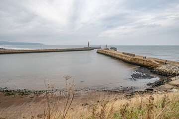 Whitby, Yorkshire, UK – October 18 2021. A wide angle shot of the East and West piers, and their respective lighthouses of Whitby Harbour from high above