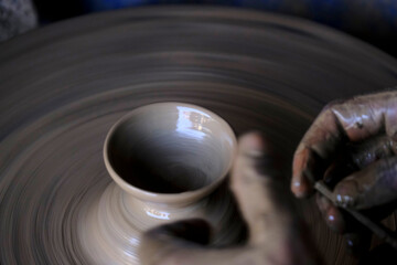 A potter prepares clay Pots or diya on potter's wheel in his residence ahead of Diwali festival. Wet and muddy hands of a craftsman shaping a clay vase on a pottery wheel.