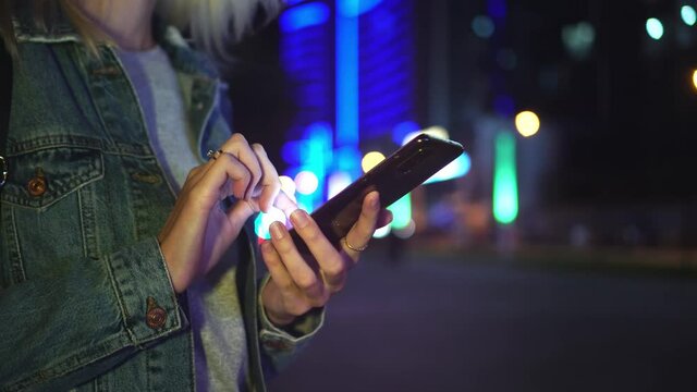 woman uses a smartphone to communicate, including to communicate, view SMS messages, chat and online shopping in the city at night: An image of gimbal. against backdrop of skyscrapers and city lights.