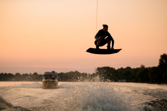 active man flying over splashing wave on wakeboard holding on to the rope. Water sports activity.