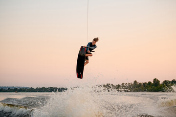 energy man engaged in water sport and jumping on splashing wave on a wakeboard