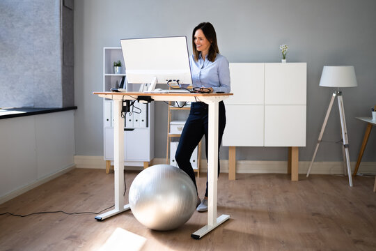 Woman Using Adjustable Height Standing Desk In Office