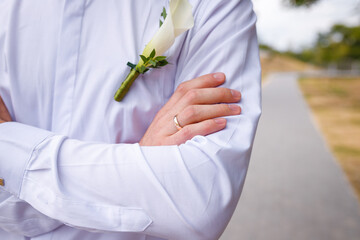 Groom in white shirt with calla lilie boutonniere, hand with golden wedding ring on finger, just married close up shot © elenaseiryk