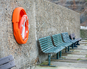 Orange life saver on the concrete wall beside wooden outdoor seating on Whitby East Pier