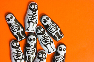 Trick or treat chocolate candies in the shape of black and white skeletons on bright orange background with copy space. Halloween sweets and treats. Celebration on October 31st. Finny scary characters