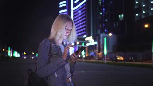 woman uses a smartphone to communicate, including to communicate, view SMS messages, chat and online shopping in the city at night: An image of gimbal. against backdrop of skyscrapers and city lights.