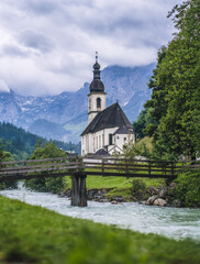 Fototapeta na wymiar A wood bench with parish church, river abd mountains in background. berchtesgaden, Ramsau Germany
