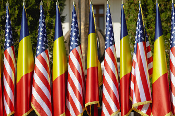 United States and Romanian flags on poles one next to another.