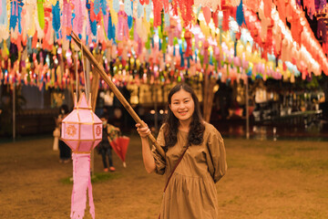Obraz na płótnie Canvas happy Asian woman holding handcraft paper lantern on wooden stick for handing in annual lantern hanging tradition in northern Thailand at night at Phra That Hariphunchai Temple, Lamphun 