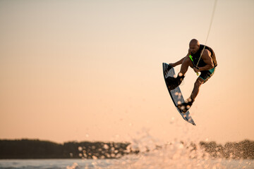 energy muscular sportsman making trick in jump time with wakeboard against the backdrop of the sky