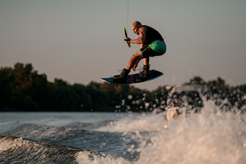 Athletic strong muscular man masterfully jumping on splashing wave on wakeboard