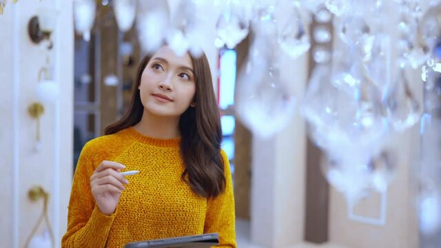 smart asian female business owner entrepreneur using tablet inventory stock checking at chandelier warehouse showroom,female designer checking chadelier matching for her new house design project
