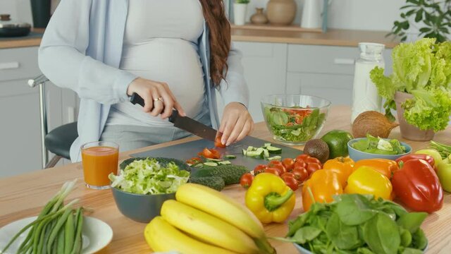 Pregnant Woman in the Kitchen Cuts Tomatoes, Prepares Dinner. Healthy, Organic and Wholesome Food. Vitamins From Fresh Vegetables for the Mother Of ohe Unborn Child. Prepare a Homemade Meal. Close-up.