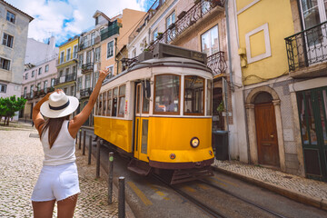 Woman and tram. Young woman tourist enjoying Lisbon city old town and waving to the famous retro yellow tram. Tourist attraction. Vacation and travel concept - obrazy, fototapety, plakaty