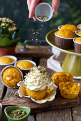 Pumpkin muffins and cupcake with white chocolate and walnuts. Side view, wooden and green background. Hand pours pumpkin seeds onto a cupcake.