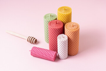 Group of natural beeswax candles of different colors and sizes on pink background. Decorative candles