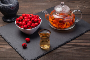 hawthorn tea in a transparent teapot and hawthorn berries in a bowl on a slate board