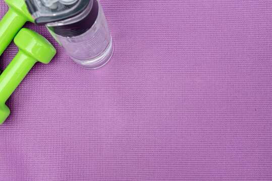 Ladie's Dumbbells And Water Bottle Over Purple Fitness Mat, Top View.