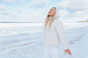 Woman wearing white clothes feels the cold on winter coast. Female breathe with cold fresh air