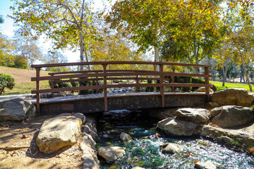 a gorgeous shot of an arched wooden bridge over a river with water rushing over rocks surrounded by...
