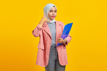 Portrait of a beautiful woman with a folder standing and making phone call on yellow background