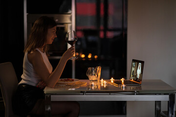 A girl sits in the kitchen in the evening drinking wine and talks via video link with her man
