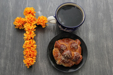 Hot coffee in an artisan cup with fluffy and delicious bread of the dead with sesame in offering of the Day of the Dead with decoration of cempasuchil and colored cut-out paper and candles
